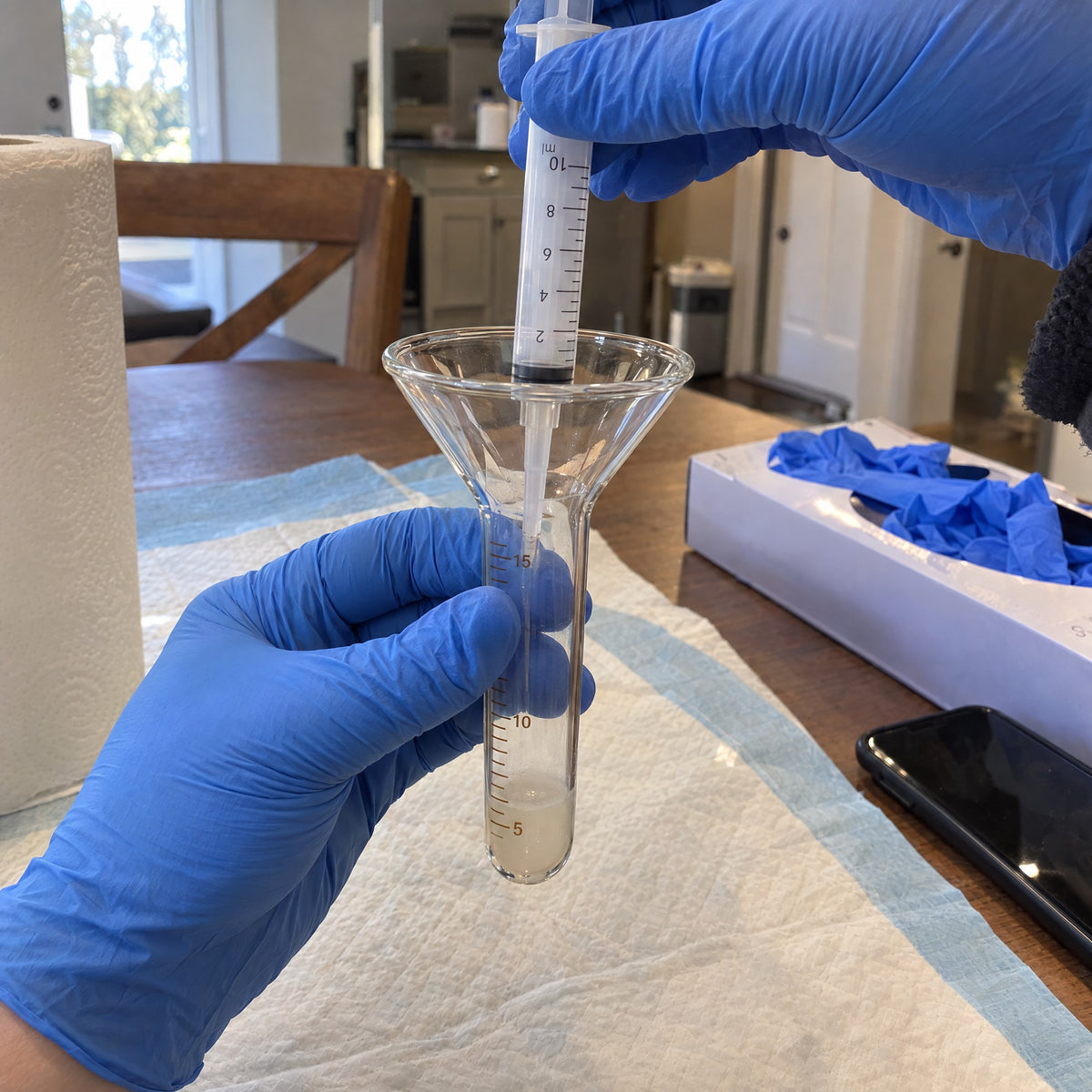 Gloved hands drawing a sample from the Kiba Collection Cup into a 10 ml syringe