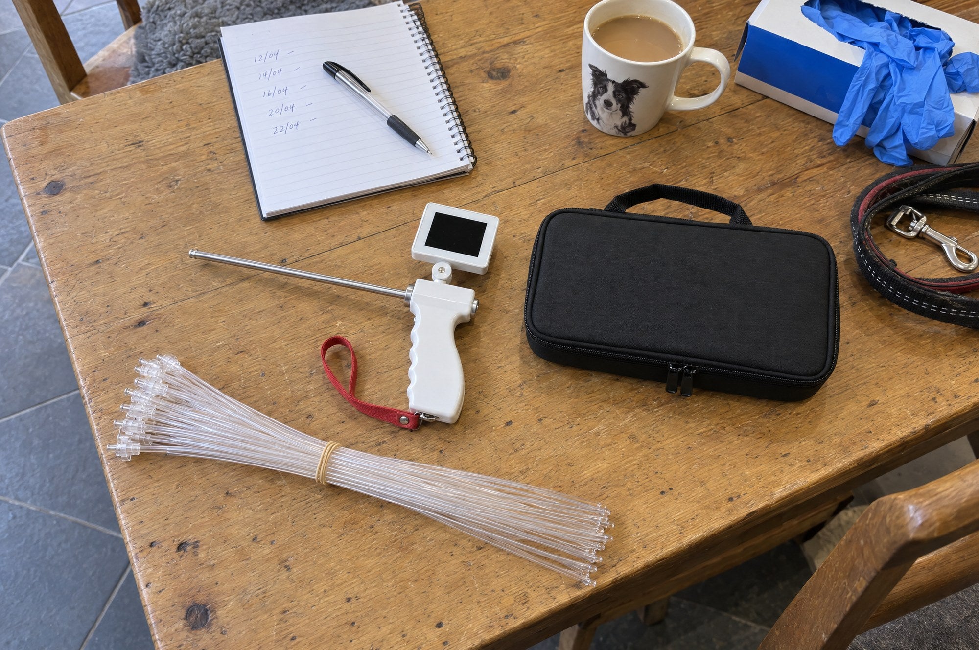 A bundle of clear insemination tubes beside the Kiba Scope and its closed carry case on an oak table